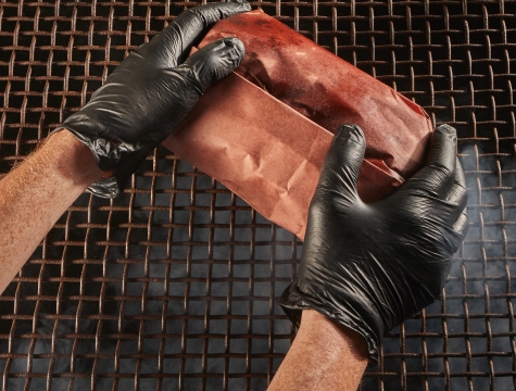 Person placing meat wrapped in butcher paper on a smoker