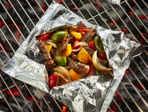 aluminum foil pack filled with beef, bell peppers and onions sitting on a grill grate