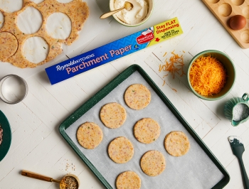 Cookies being cut out of dough to be placed on a parchment lined baking sheet