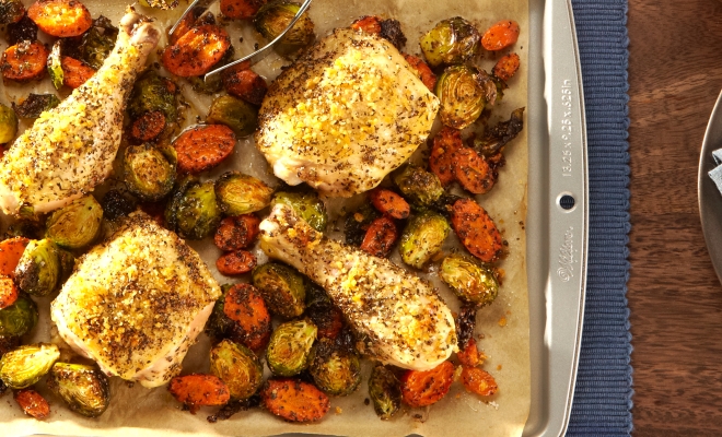 Roasted chicken and vegetables sitting on a parchment lined baking sheet